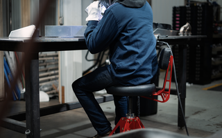 person sitting in red and block shop chair working on car in garage