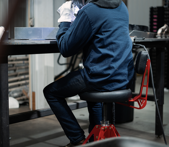 person sitting in red and block shop chair working on car in garage